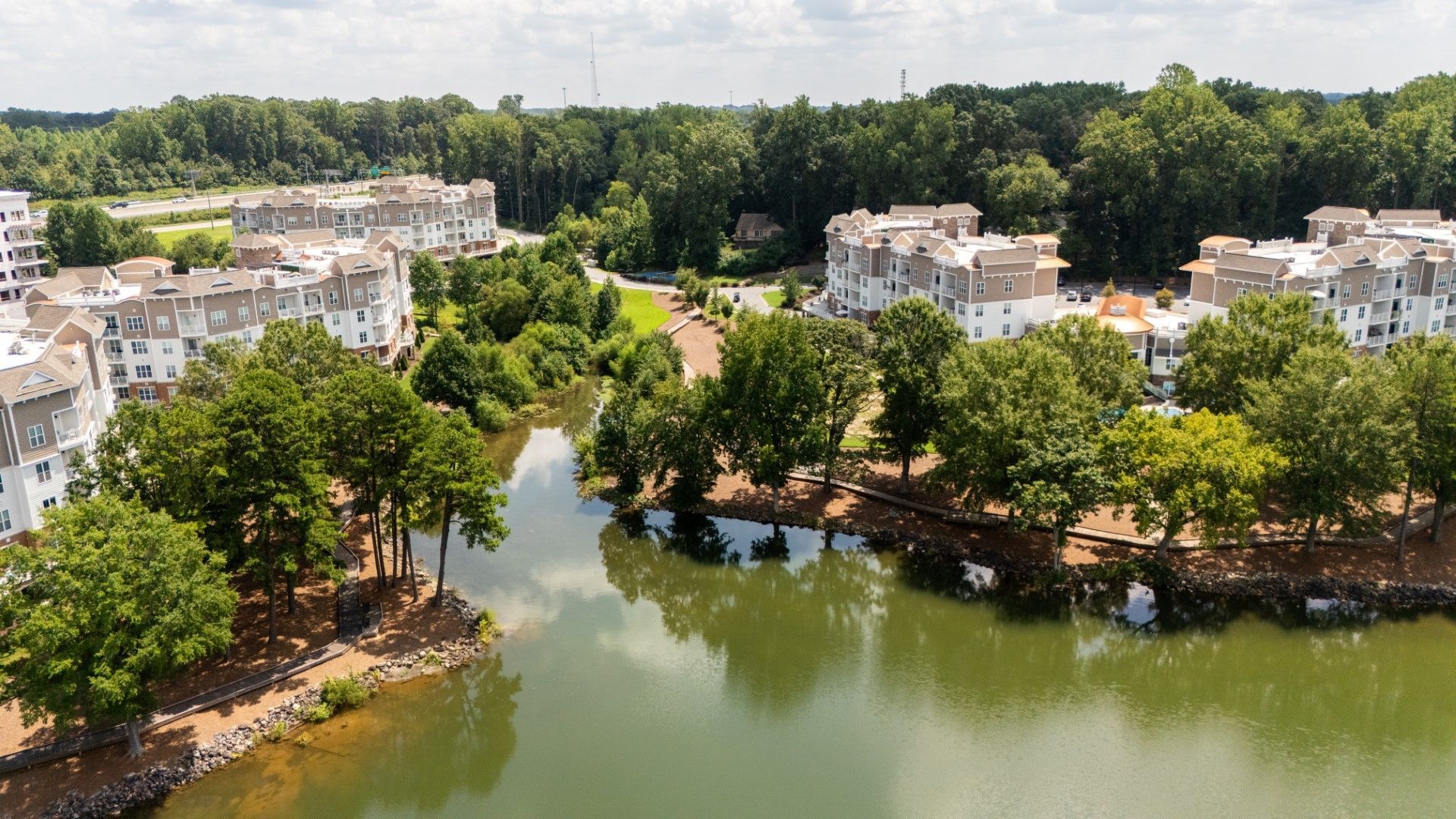 Aerial view of a lakeside residential area with white buildings, trees, and a winding green canal