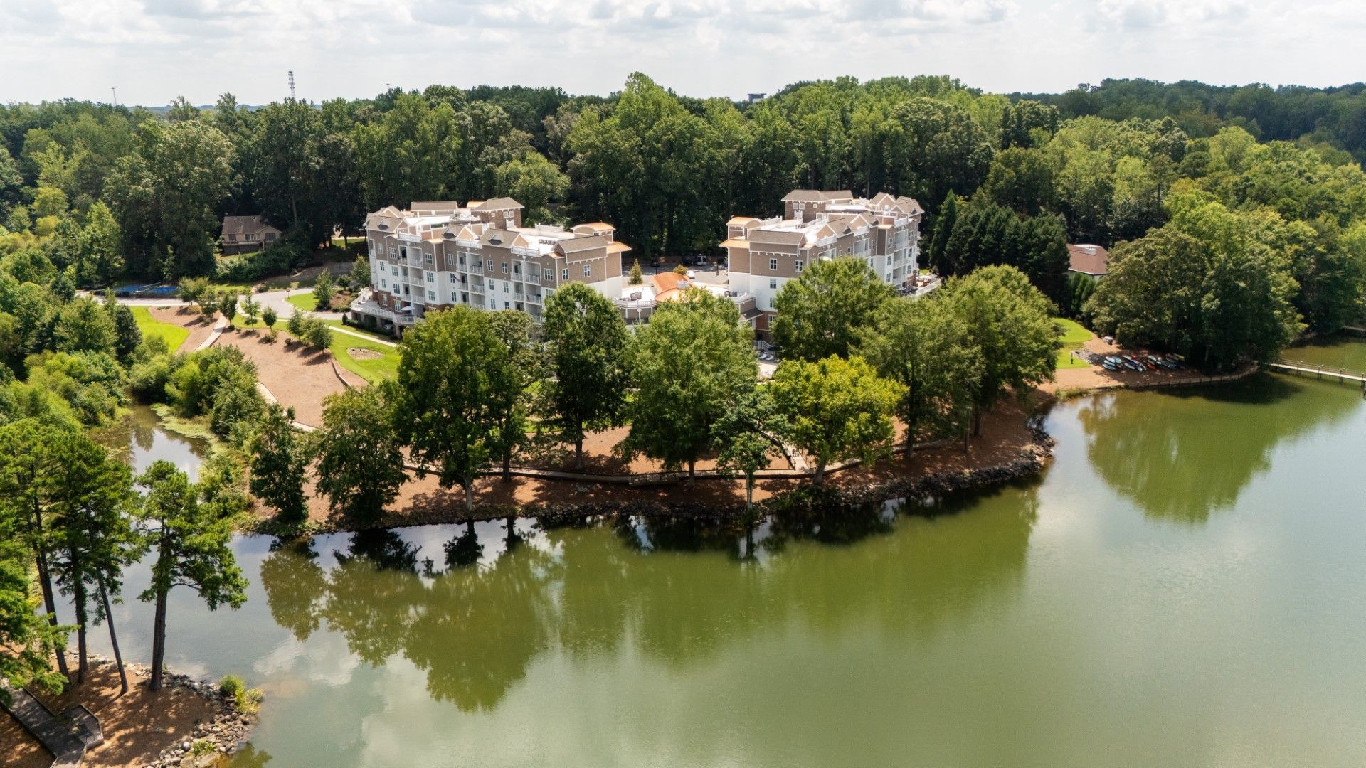Aerial view of white lakeside buildings surrounded by trees beside a calm green lake