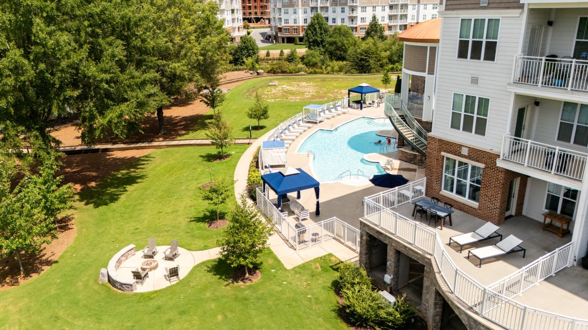Apartment courtyard with pool, patio chairs, and green lawn in bright daylight