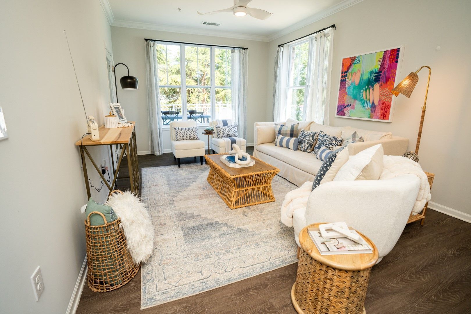 Living room with white furniture, colorful art, patterned rug, and large windows at The Osprey at Lake Norman, offering apartments for rent in Mooresville, NC.