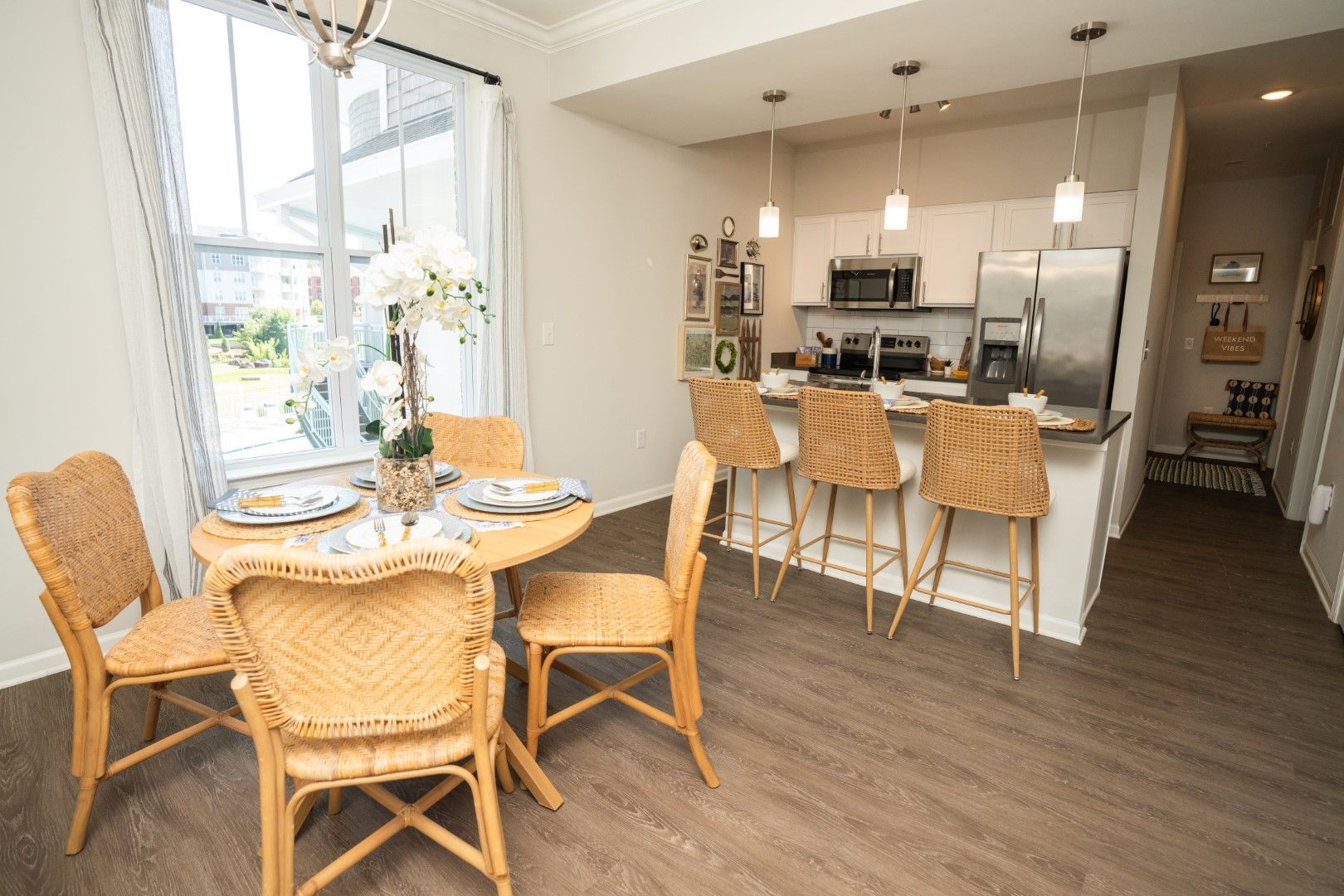 Dining area with round table and rattan chairs next to a kitchen with bar stools at The Osprey at Lake Norman, offering Mooresville apartments.
