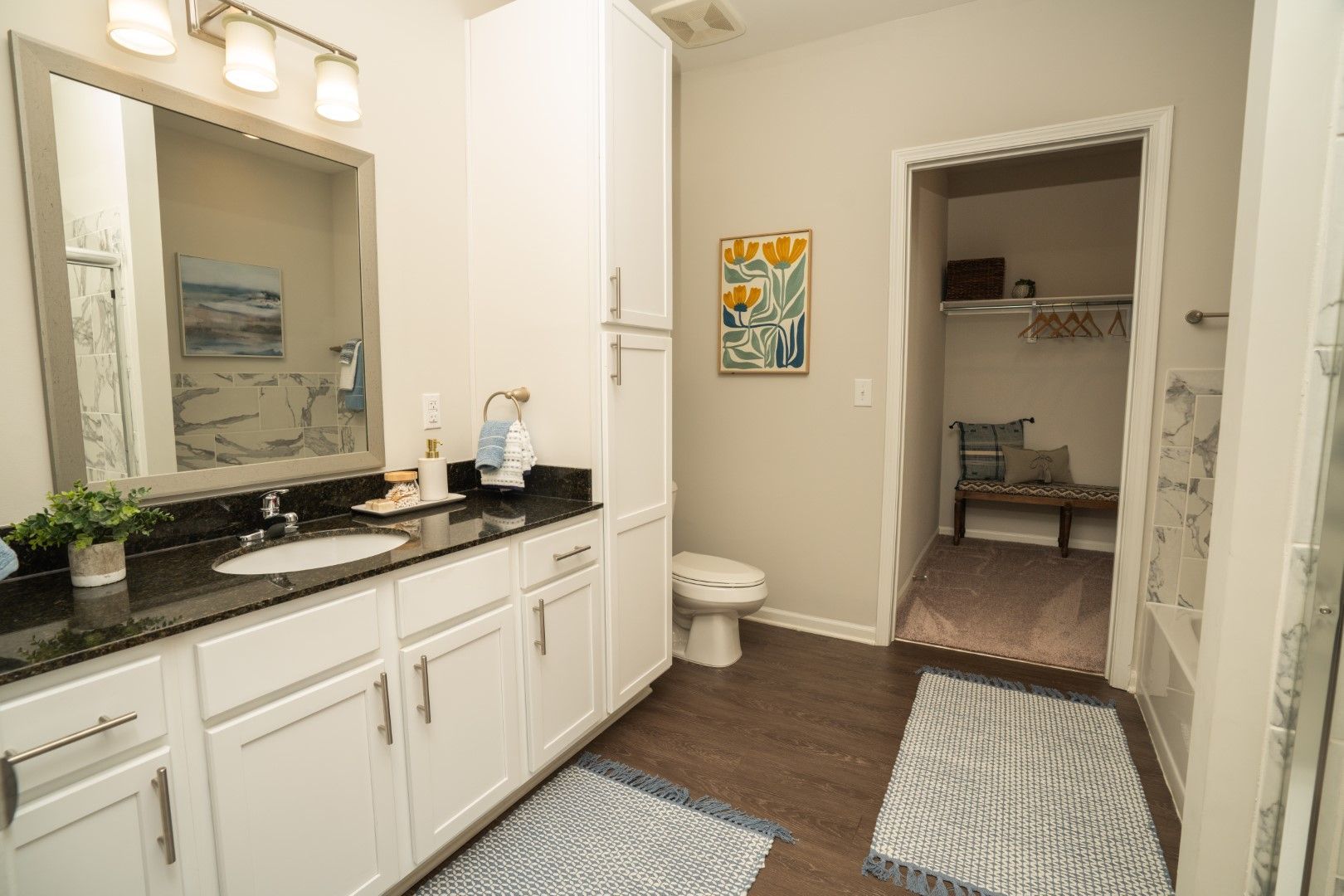 Bathroom with white cabinets, dark countertop, and wood floor at The Osprey at Lake Norman, offering Mooresville apartments for rent. A walk-in closet is open in the back.
