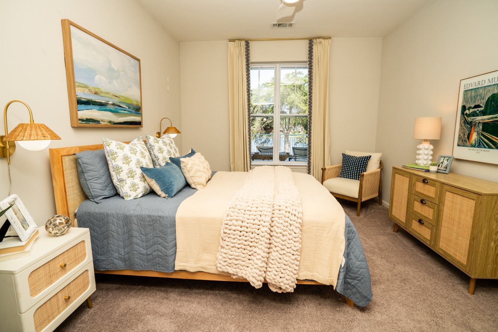 Bedroom with bed, nightstand, dresser, and armchair at The Osprey at Lake Norman, offering luxury apartments in Mooresville, NC. Earthy tones with blue and cream accents.