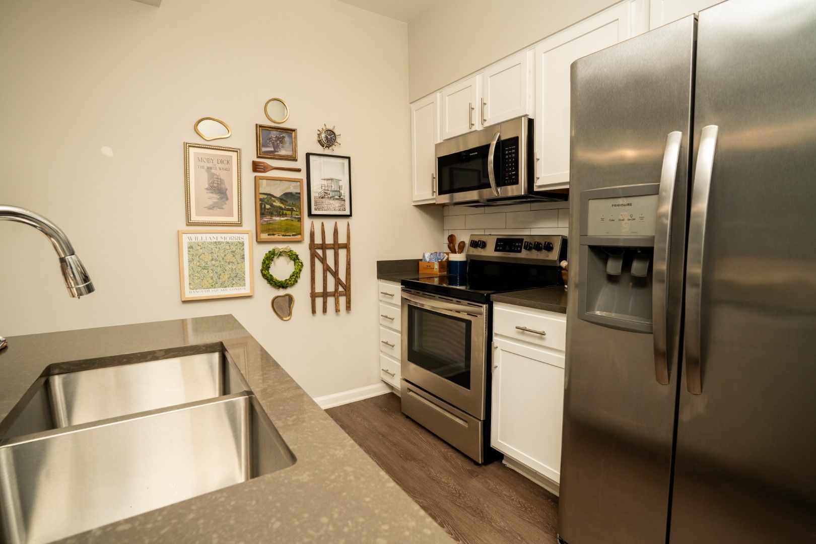 Kitchen with stainless steel appliances, white cabinets, artwork on the wall, and a double sink at The Osprey at Lake Norman, offering Mooresville apartments.