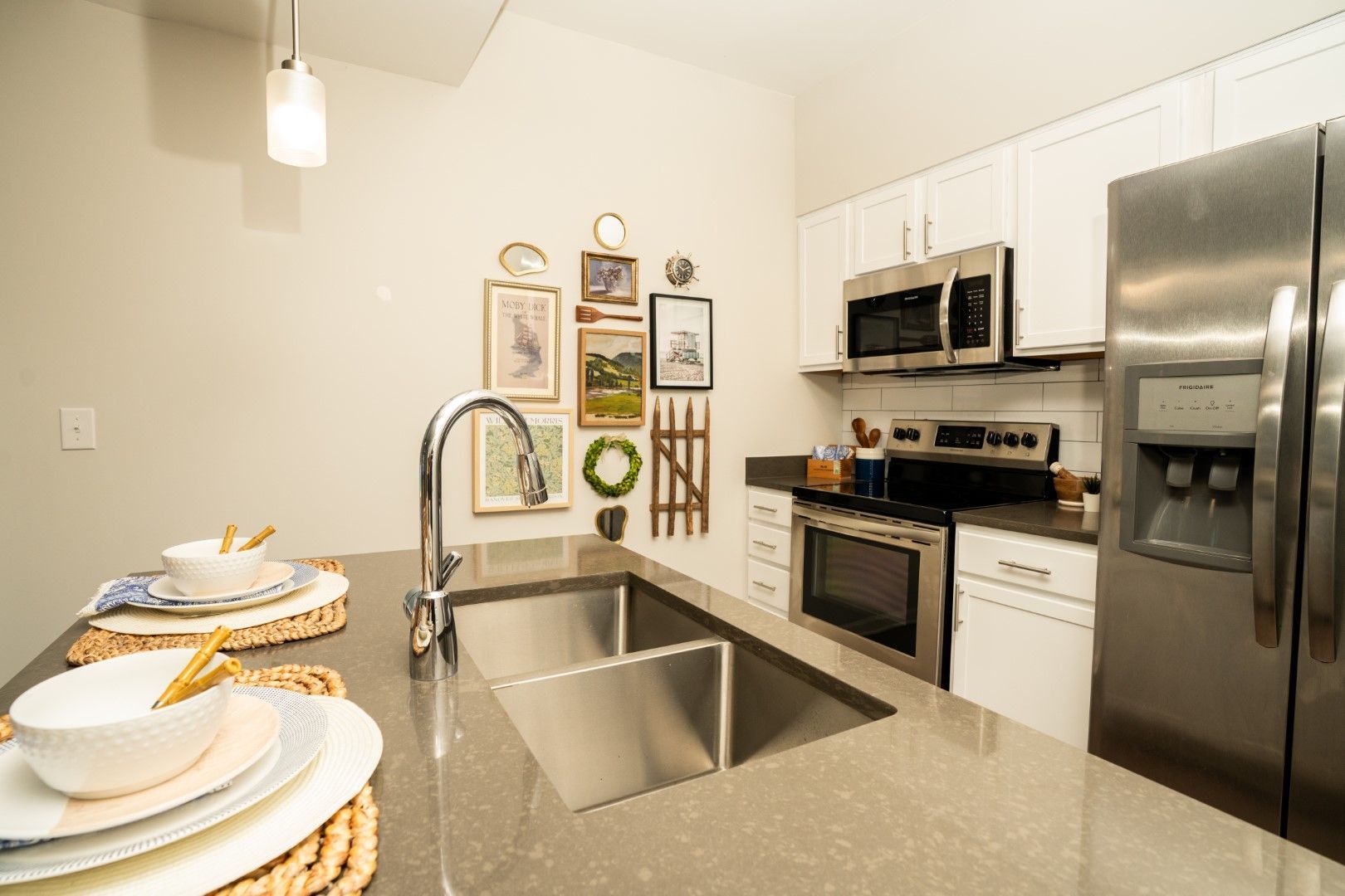 Modern kitchen with stainless steel appliances, a sink island, and framed wall art at The Osprey at Lake Norman, offering Mooresville apartments.