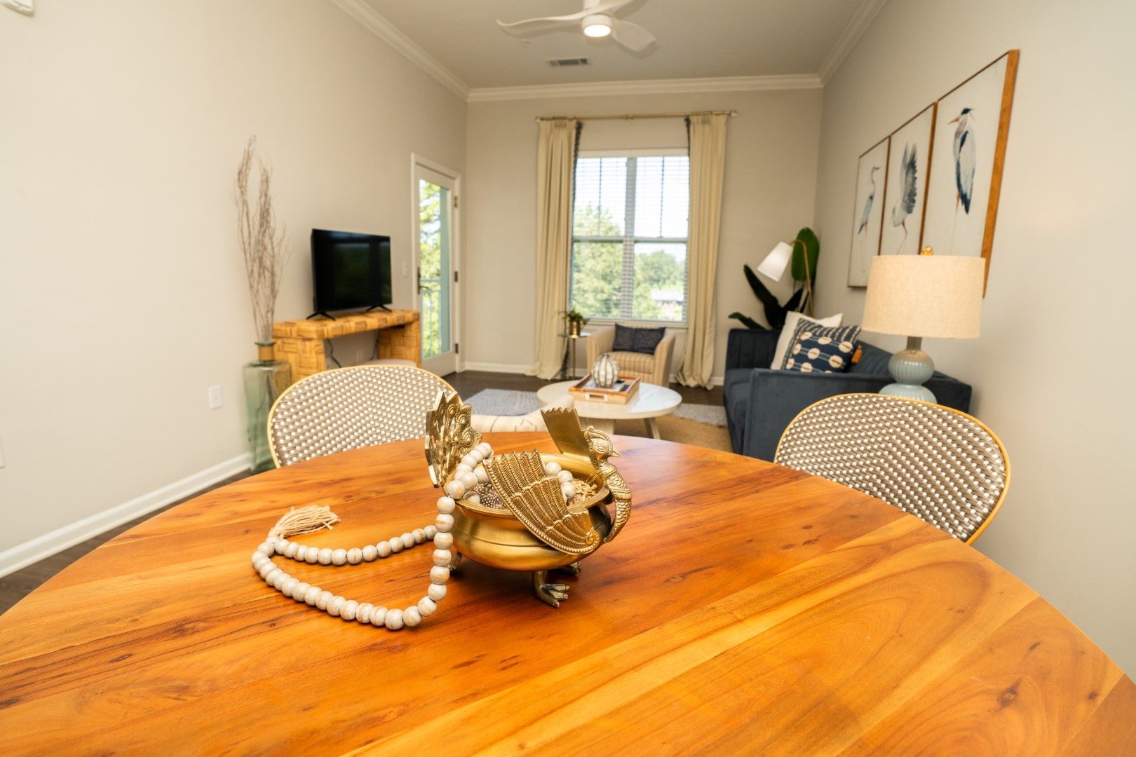 Living room with white furniture, blue accents, rattan coffee table, and colorful abstract art.