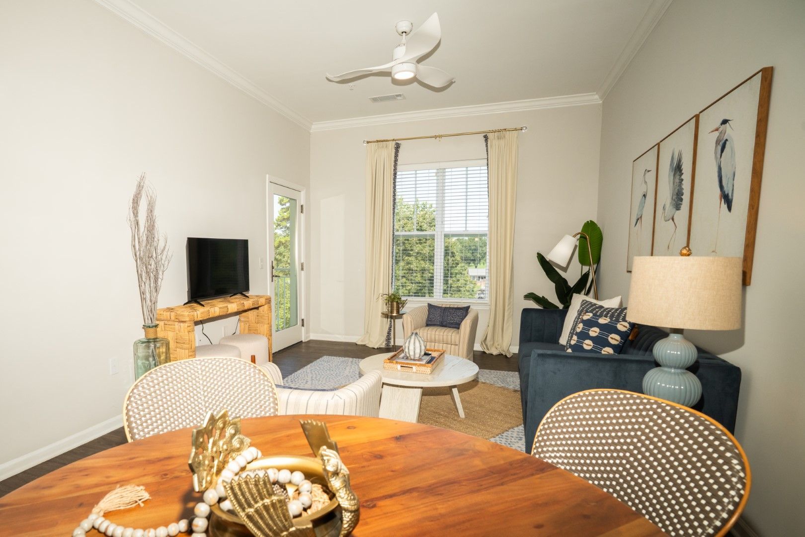 Living room with round dining table, sofa, and armchair at The Osprey at Lake Norman, offering luxury apartments in Mooresville, NC. Neutral walls, natural light, and ceiling fan.