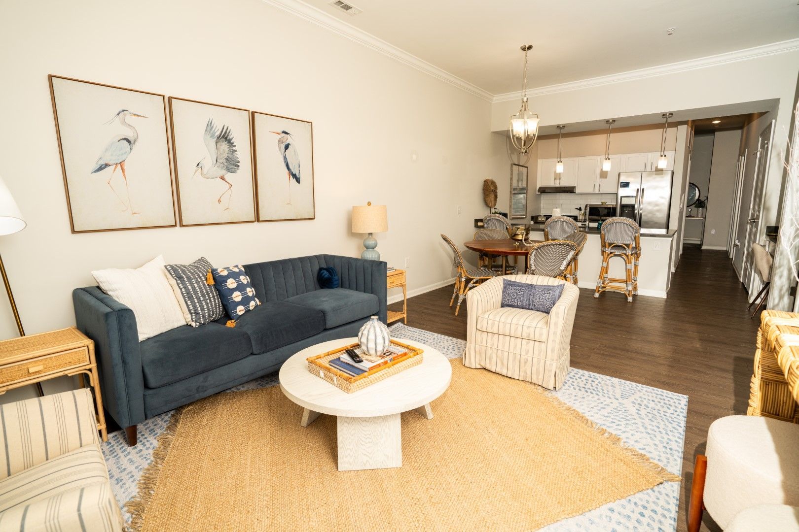 Living room with blue sofa, art, and open kitchen at The Osprey at Lake Norman, offering Mooresville apartments. Beige rug and light wood floors.