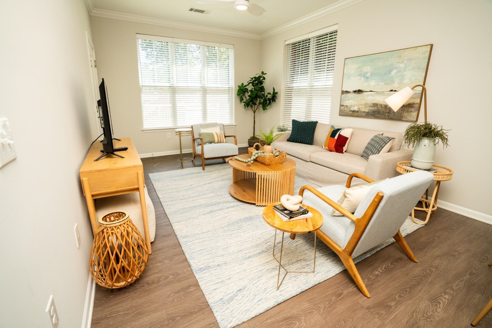 Living room with neutral tones, sofa, chairs, rug, coffee table, TV, and artwork at The Osprey at Lake Norman, offering apartments for rent in Mooresville, NC.