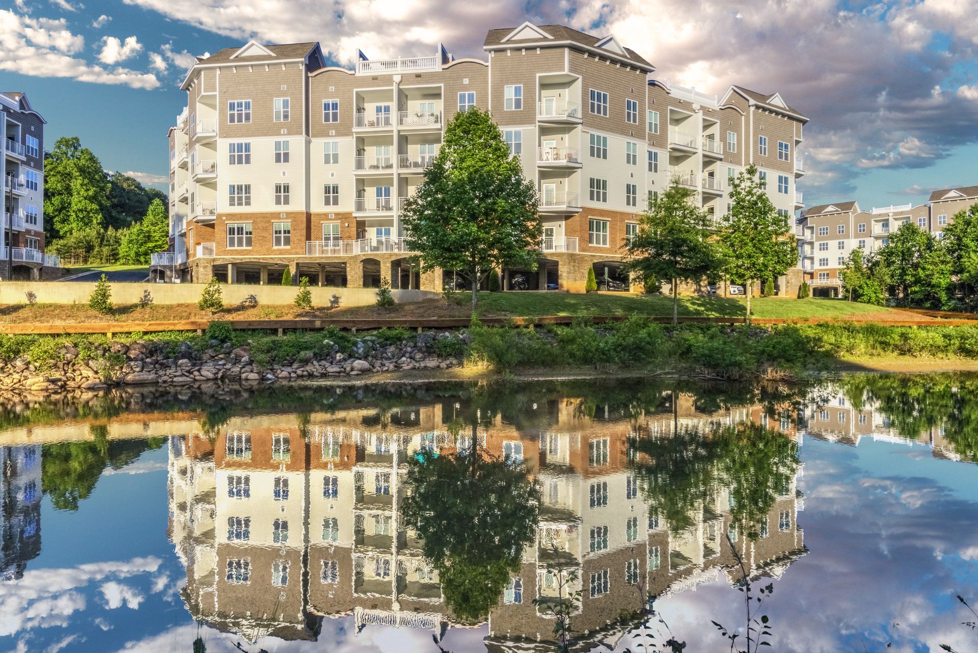 Apartment building reflected in a still pond under a blue sky with clouds.