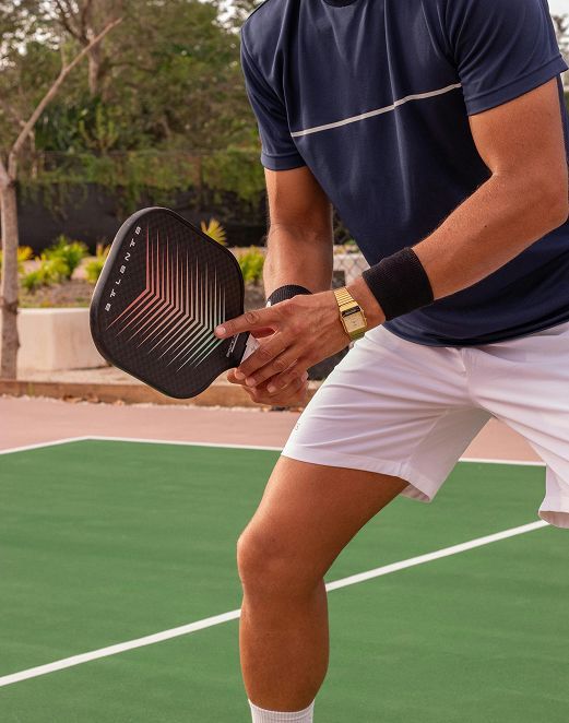Person holding a black pickleball paddle on an outdoor court, wearing a navy shirt and white shorts.