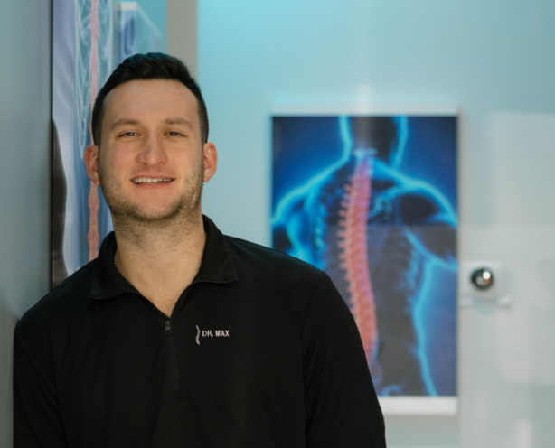 Man using a massage gun on another person’s shoulder in a bright room