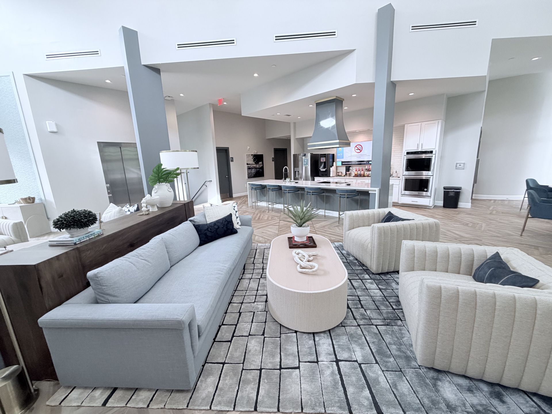Modern open-plan living room with gray and cream sofas, coffee table, and kitchen in the background