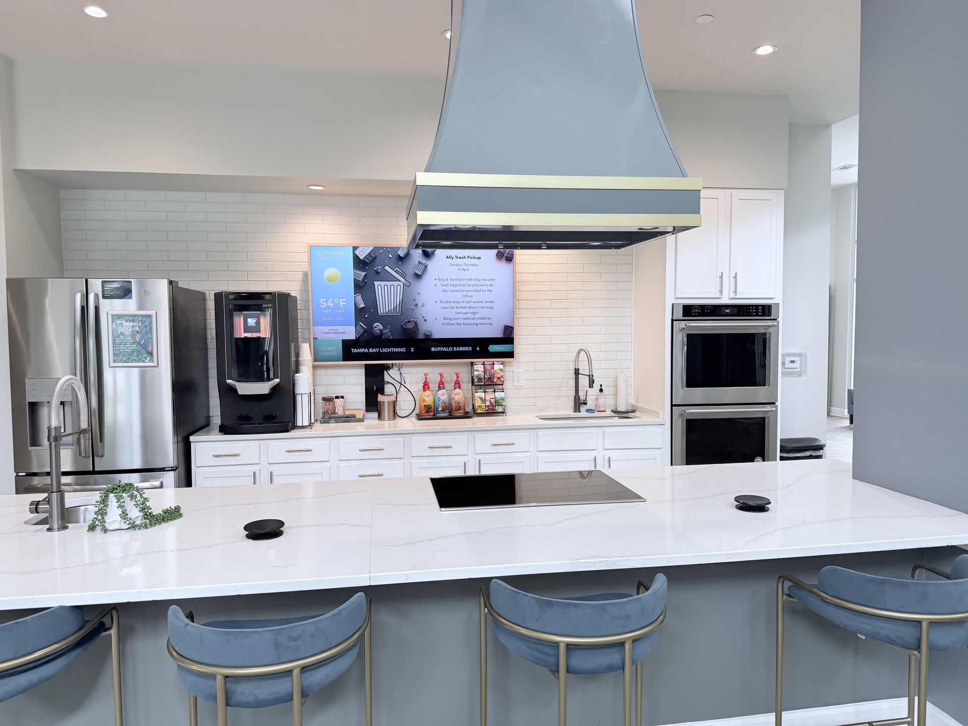 Modern white kitchen with island, blue stools, stainless appliances, and a large range hood