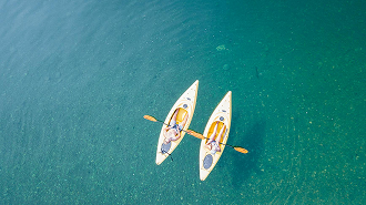 Two people kayaking in white kayaks on clear blue water, seen from above
