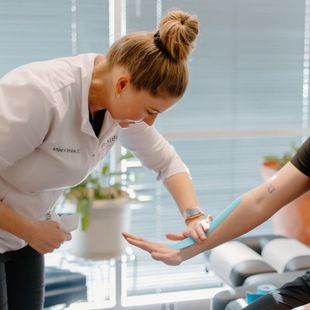 A woman in a white shirt with a bun on her head is examining a patient 's arm