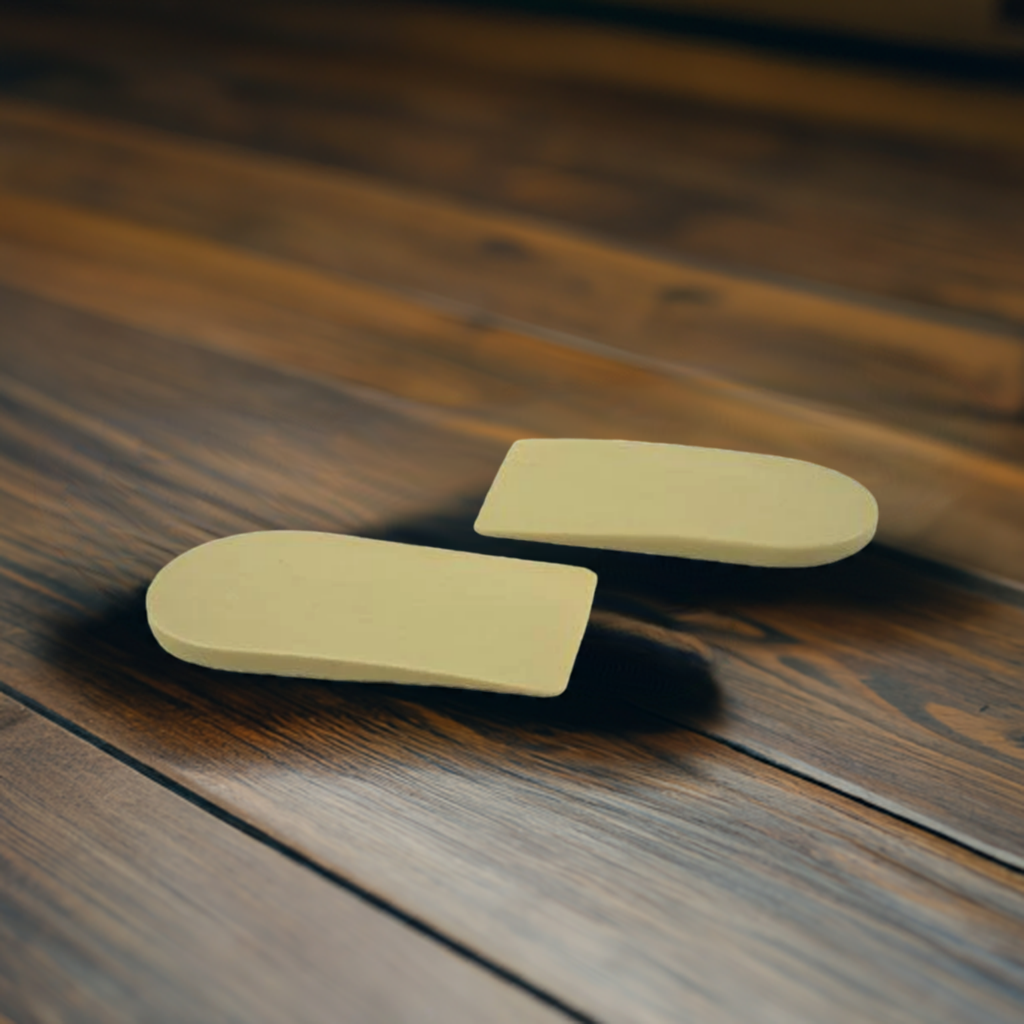 A pair of yellow heel lift insert insoles are sitting on a wooden floor.
