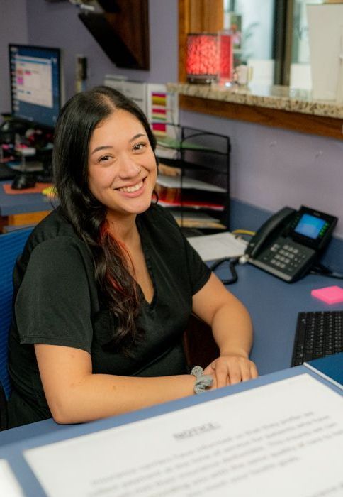 A woman in a black shirt is smiling while sitting at a desk