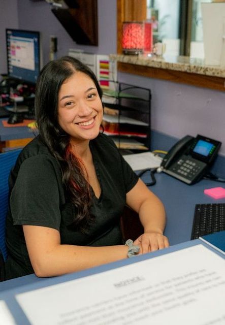 A woman in a black shirt is smiling while sitting at a desk
