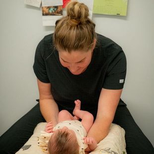 A woman is sitting on a pillow with a baby on her lap.
