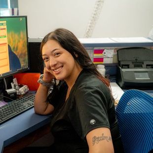 A woman with a tattoo on her arm is smiling in front of a computer