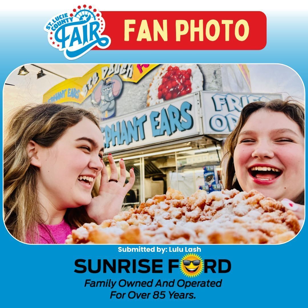 Two smiling friends at a fair eating cotton candy under the “FAN PHOTO” banner