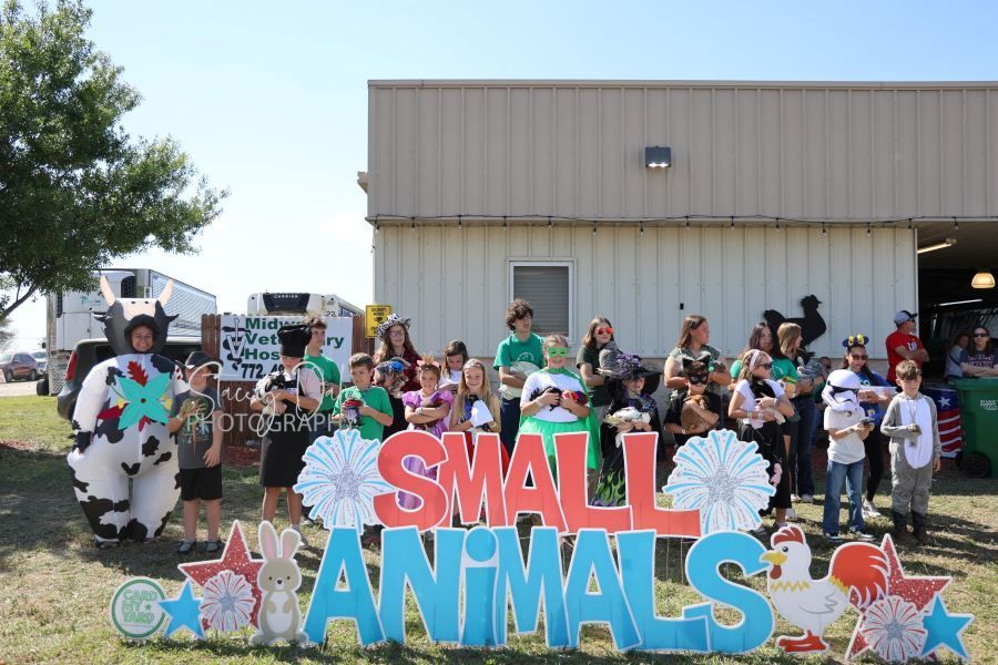 Group of children and adults posing outdoors behind a colorful “Small Animals” sign
