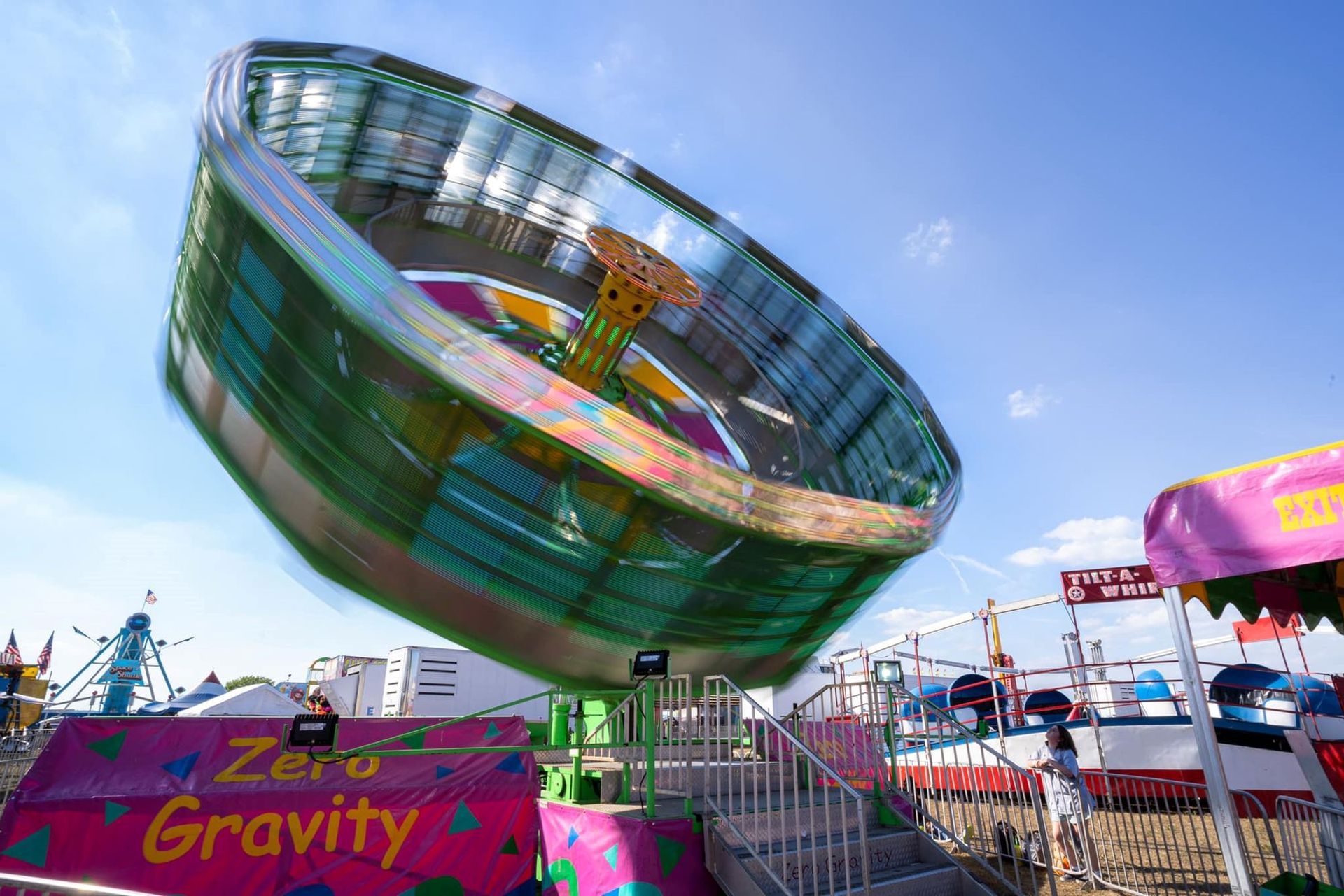 Amusement park ride spinning in the air above a colorful Zero Gravity booth under a blue sky