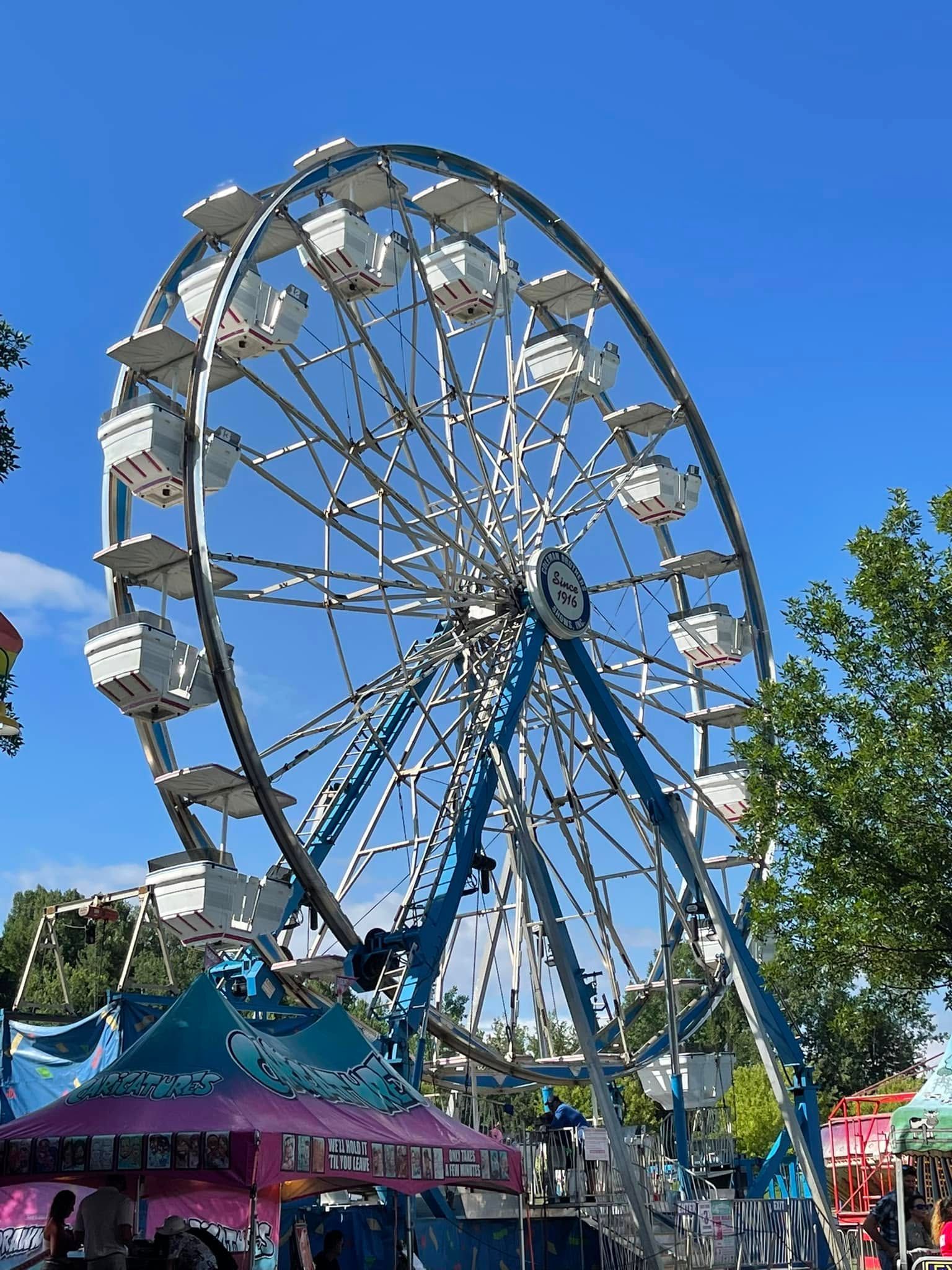 Large Ferris wheel with blue supports at an outdoor fair under a clear blue sky