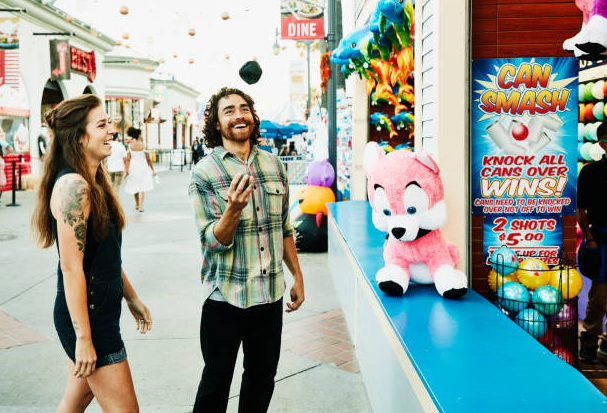 Two people smiling at a carnival game booth with colorful prizes and stuffed animals