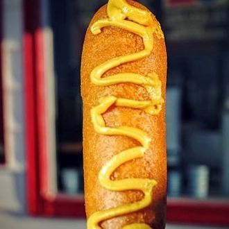 Corn dog topped with yellow mustard against a blurred background