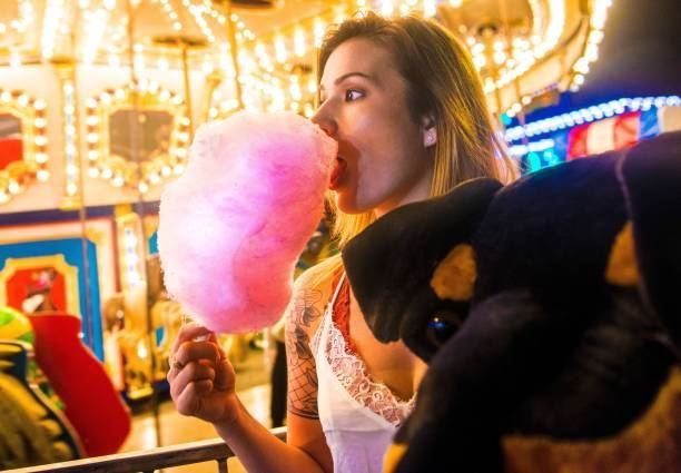 Woman eating pink cotton candy at a brightly lit carnival carousel