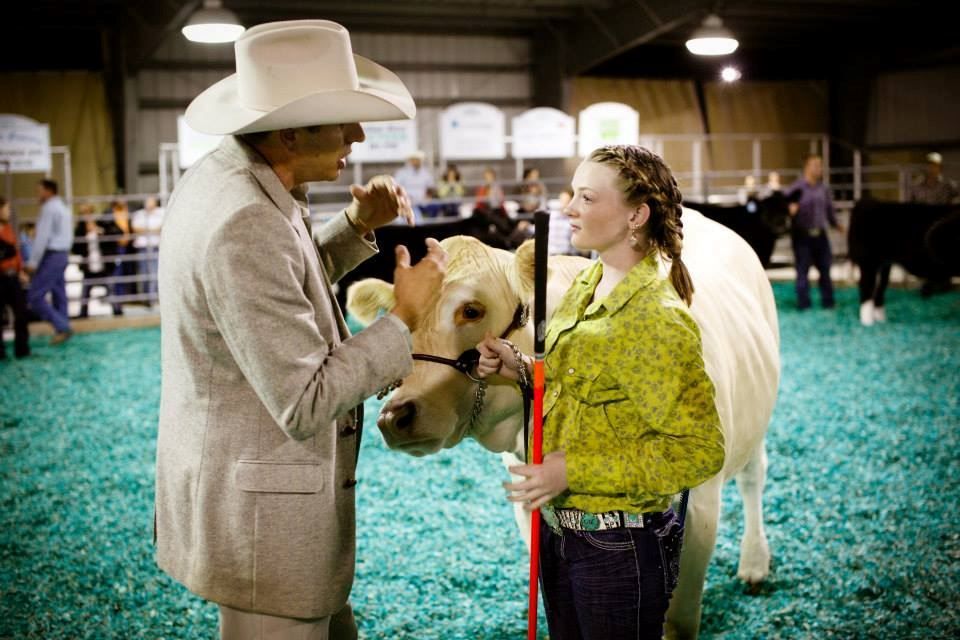 Cowboy hat-wearing man and woman with a white horse at an indoor rodeo arena