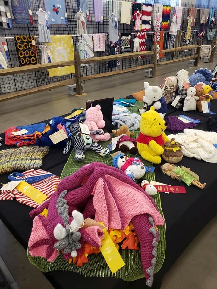 Stuffed animals and knit blankets displayed on a market table with colorful textiles in the background