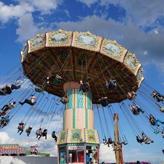 Carousel swing ride against a blue sky with riders in motion and decorative panels on the canopy