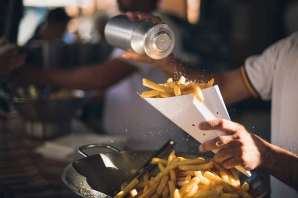 French fries being poured from a paper cone into a tray at a food stall