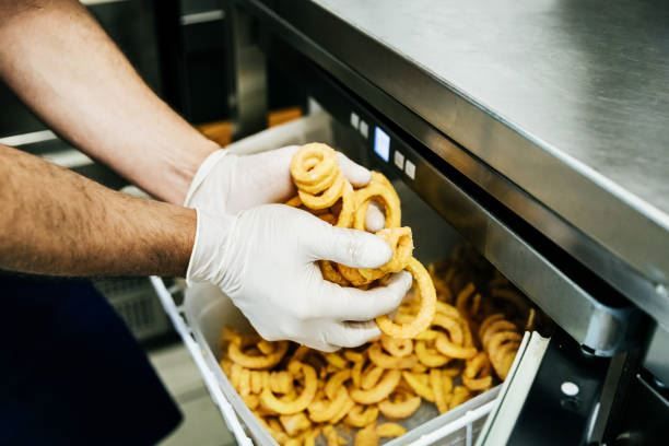 Gloved hands loading golden onion rings into a metal fryer basket in a stainless steel kitchen