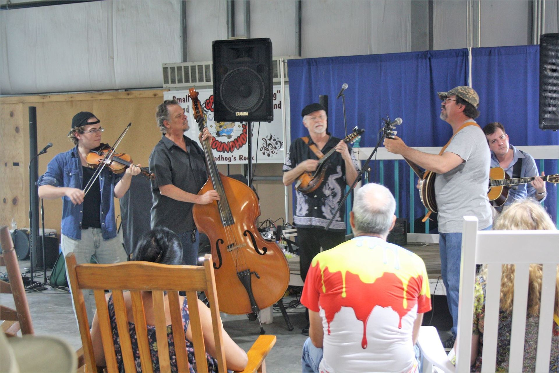 Musicians performing live indoors, with violin, cello, and guitar in front of seated audience members.