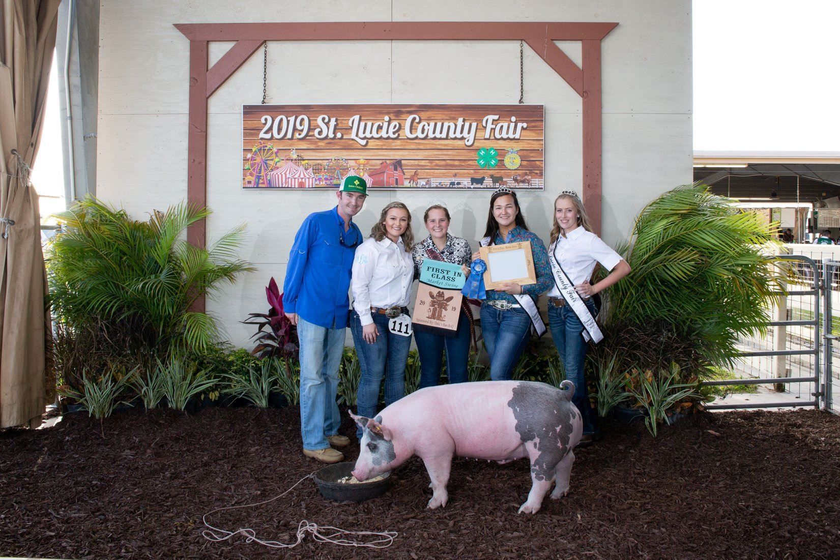 Group posing at the 2019 St. Jude Country Fair sign with a pig in front and plants around them