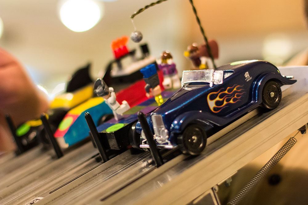 Toy race cars lined up on a track, including a blue car with flame decals in front.