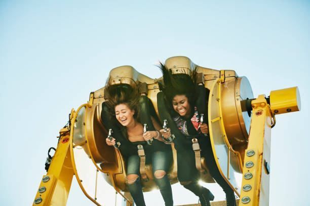 Two people riding a spinning amusement ride, smiling against a blue sky.