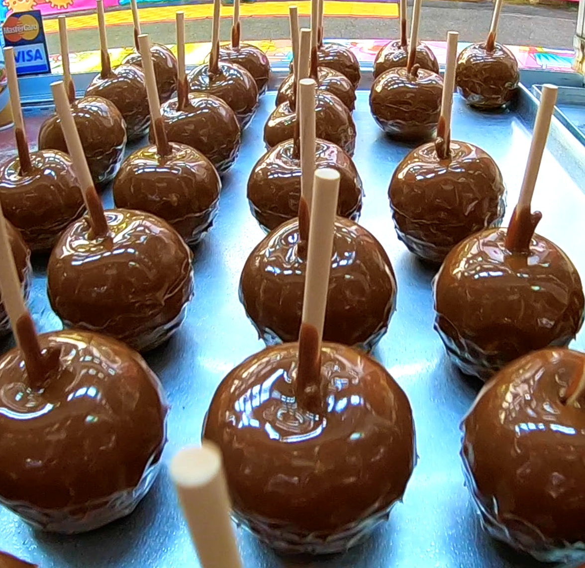 Rows of glossy caramel apples on sticks, displayed on a tray at a market stall.
