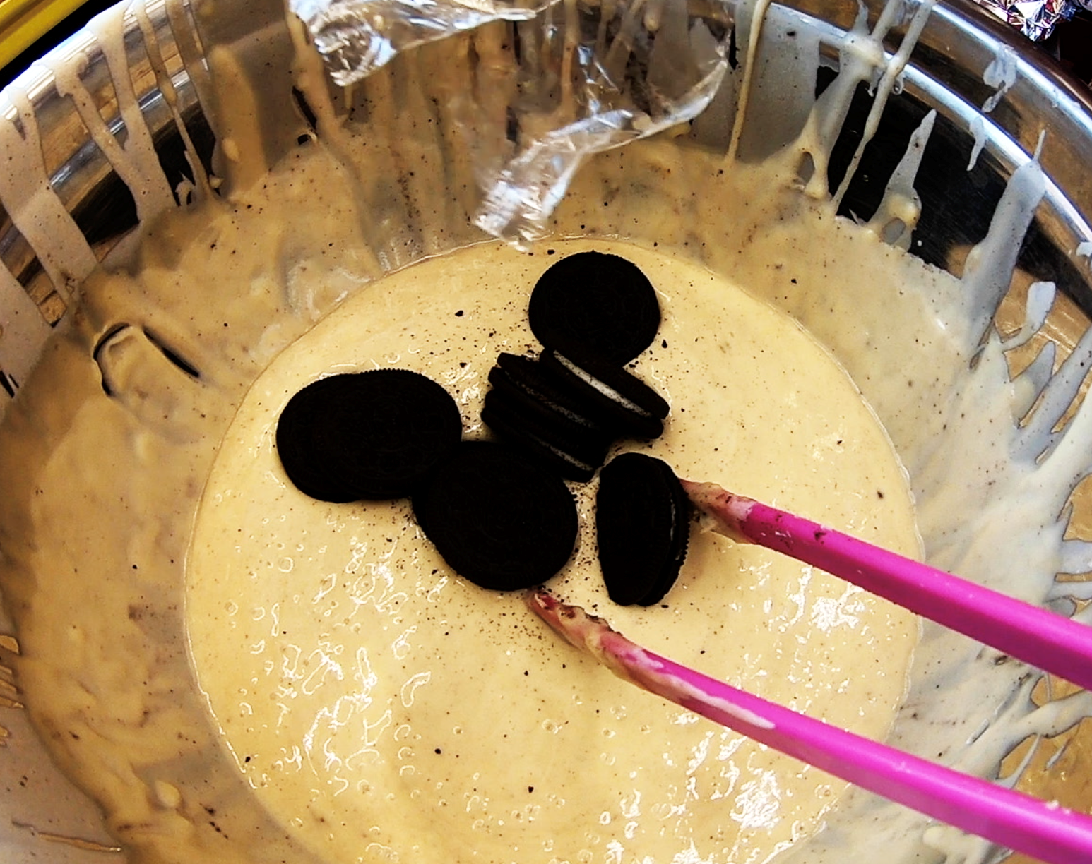 Pink chopsticks holding black-coated candies over a bowl of pale batter