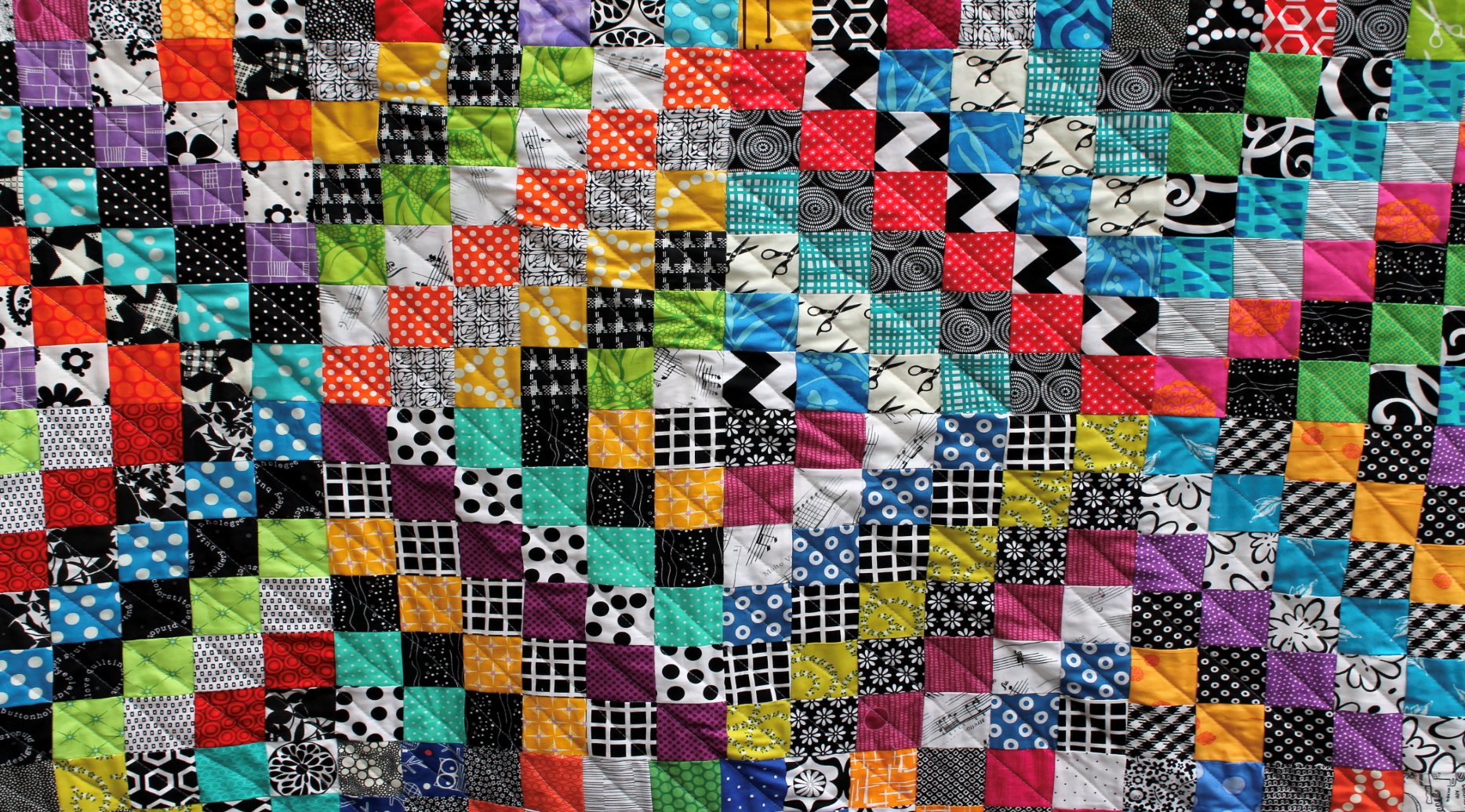 Colorful patchwork quilt with many patterned squares and diagonal red-and-black accents