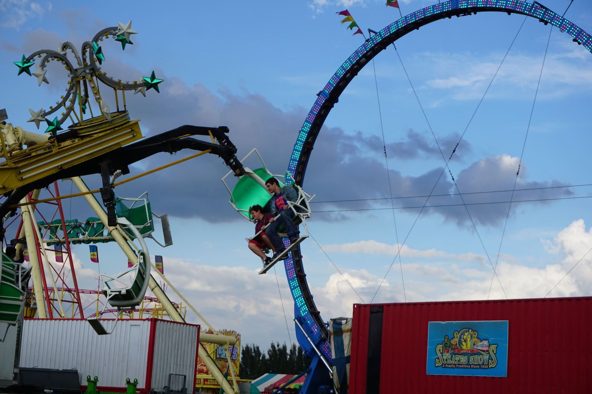 Person riding a tall blue swing ride at an amusement park, with cloudy sky and carnival structures nearby