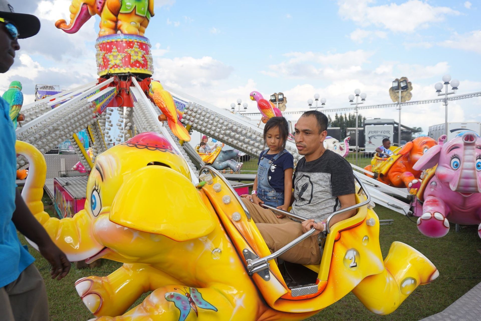 Children riding a yellow amusement-park ride with a pink animal car on a sunny day