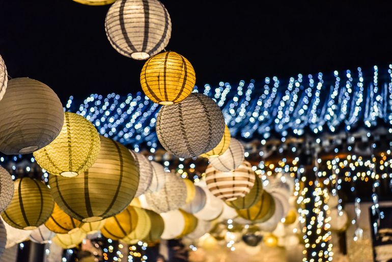 String-lit paper lanterns hanging at night, with blue and warm white lights in the background