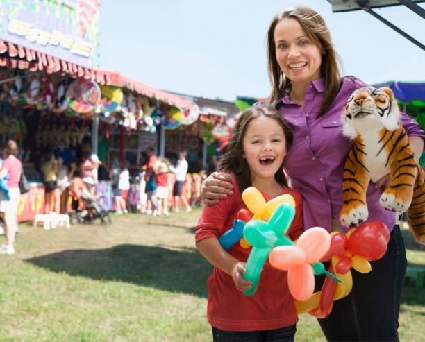 Woman and child smiling at a fair, holding colorful balloon flowers and a tiger plush toy.