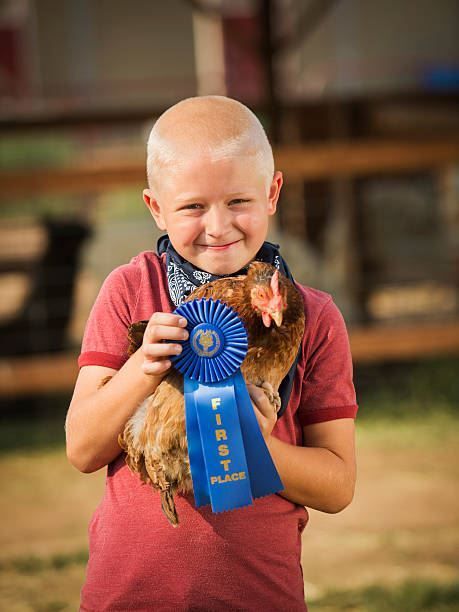 Smiling child in red shirt holding a chicken with a blue ribbon award