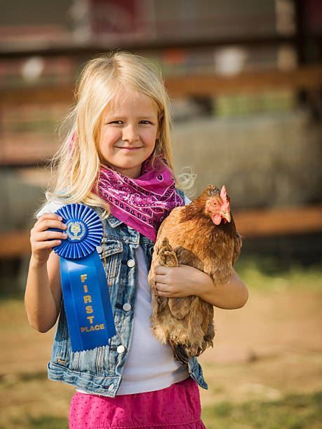 Girl holding a brown chicken and a blue ribbon outdoors, smiling at the camera